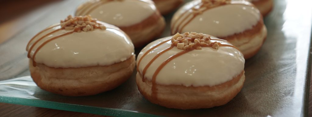 Cream filled doughnuts covered in vanilla icing drizzled with maple and a sprinkle of crushed walnuts added on top.