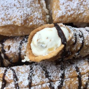 Cannoli covered in powdered sugar and drizzled with chocolate.